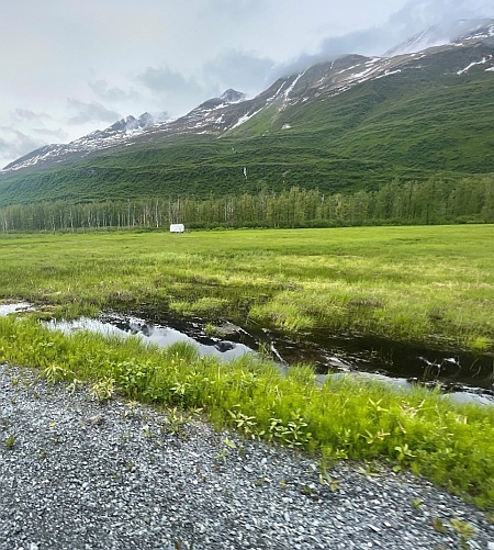 Standing water in a low-lying area with vegetation and mountains on one side and a gravel road on the other.